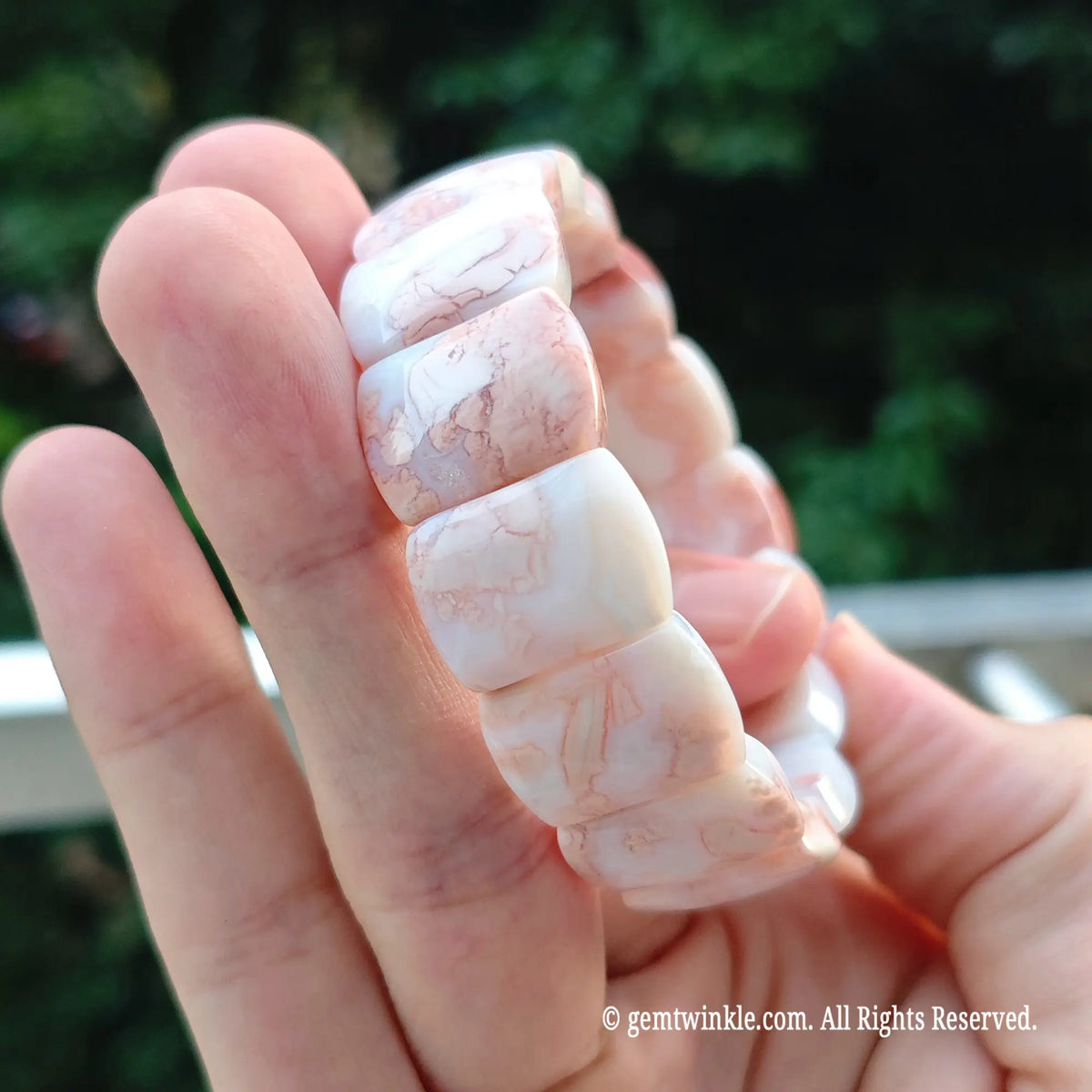 Perspective shot of stacked pink agate plate bead cuff held across fingers under natural daylight