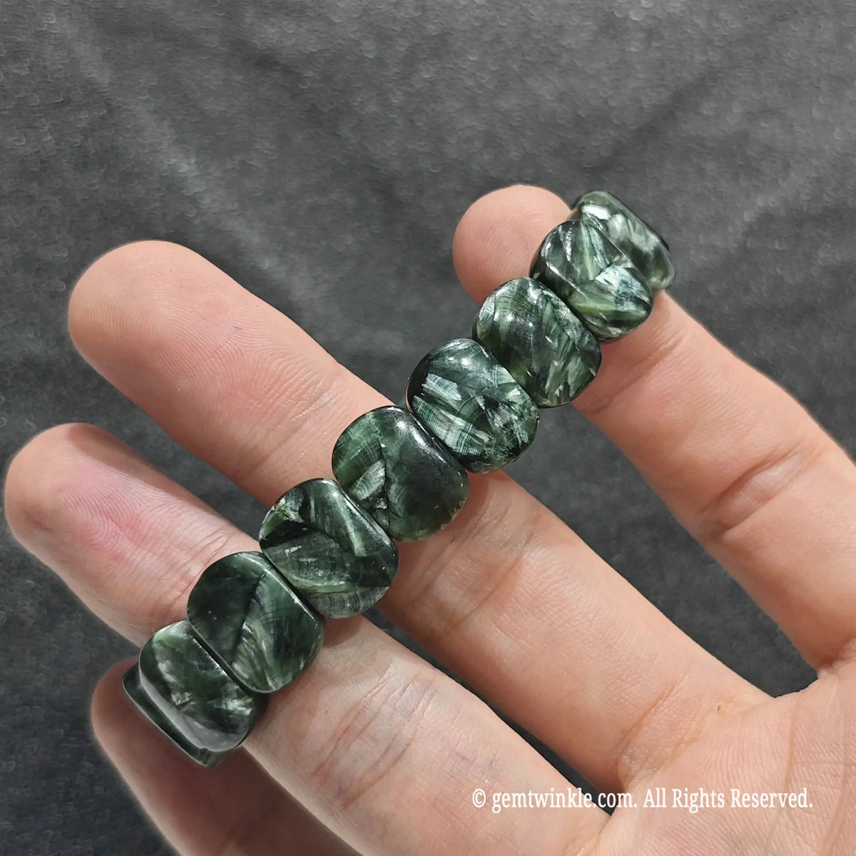 Perspective shot of stacked seraphinite flat bead strand resting across fingers under studio lighting