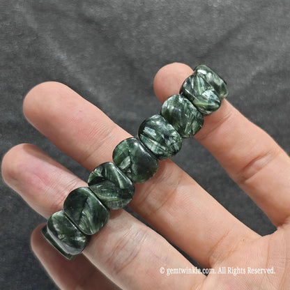 Perspective shot of stacked seraphinite flat bead strand resting across fingers under studio lighting