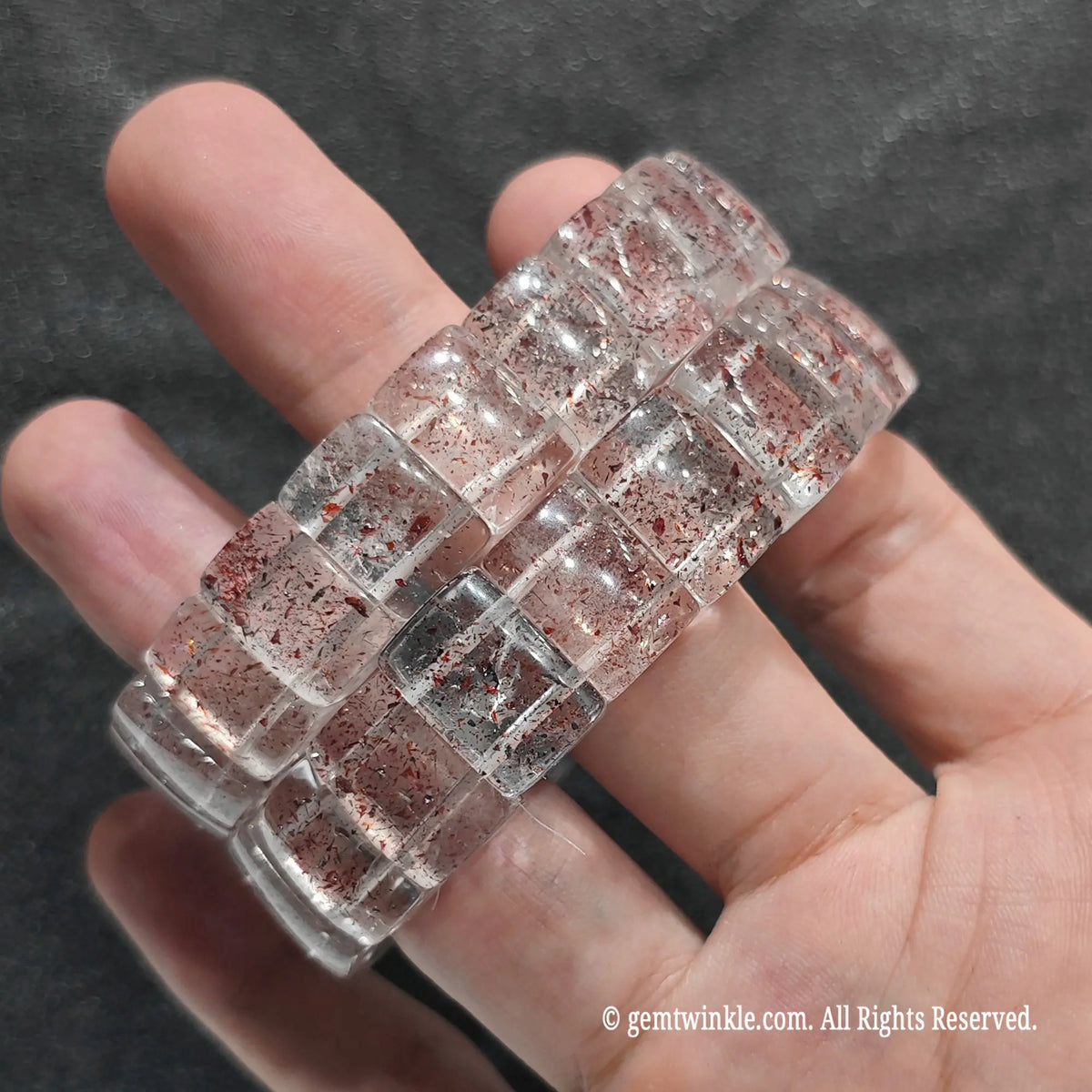 Perspective shot of stacked strawberry quartz rectangular bead wristband resting across fingers