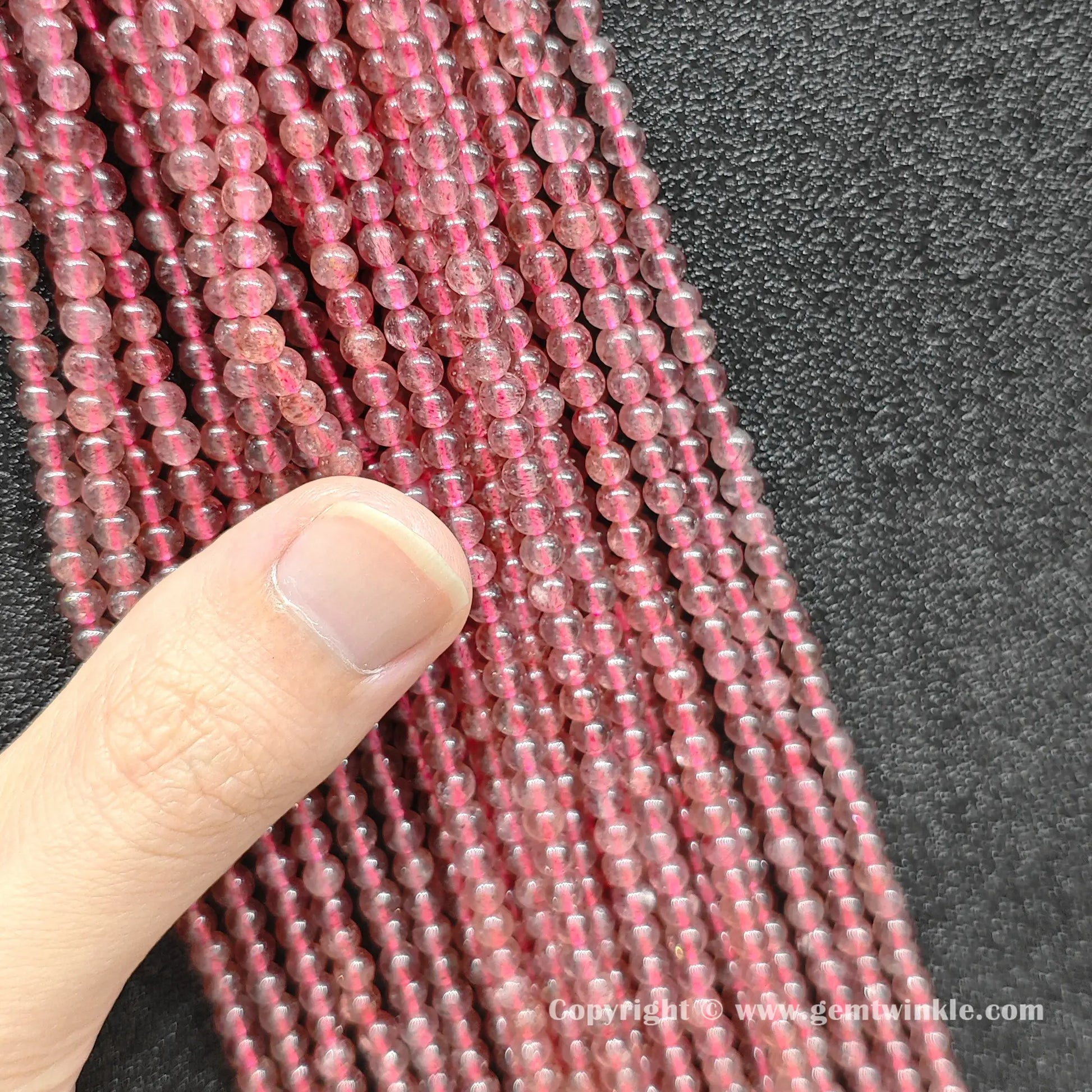 Natural translucent strawberry quartz bead strands held in hand for scale