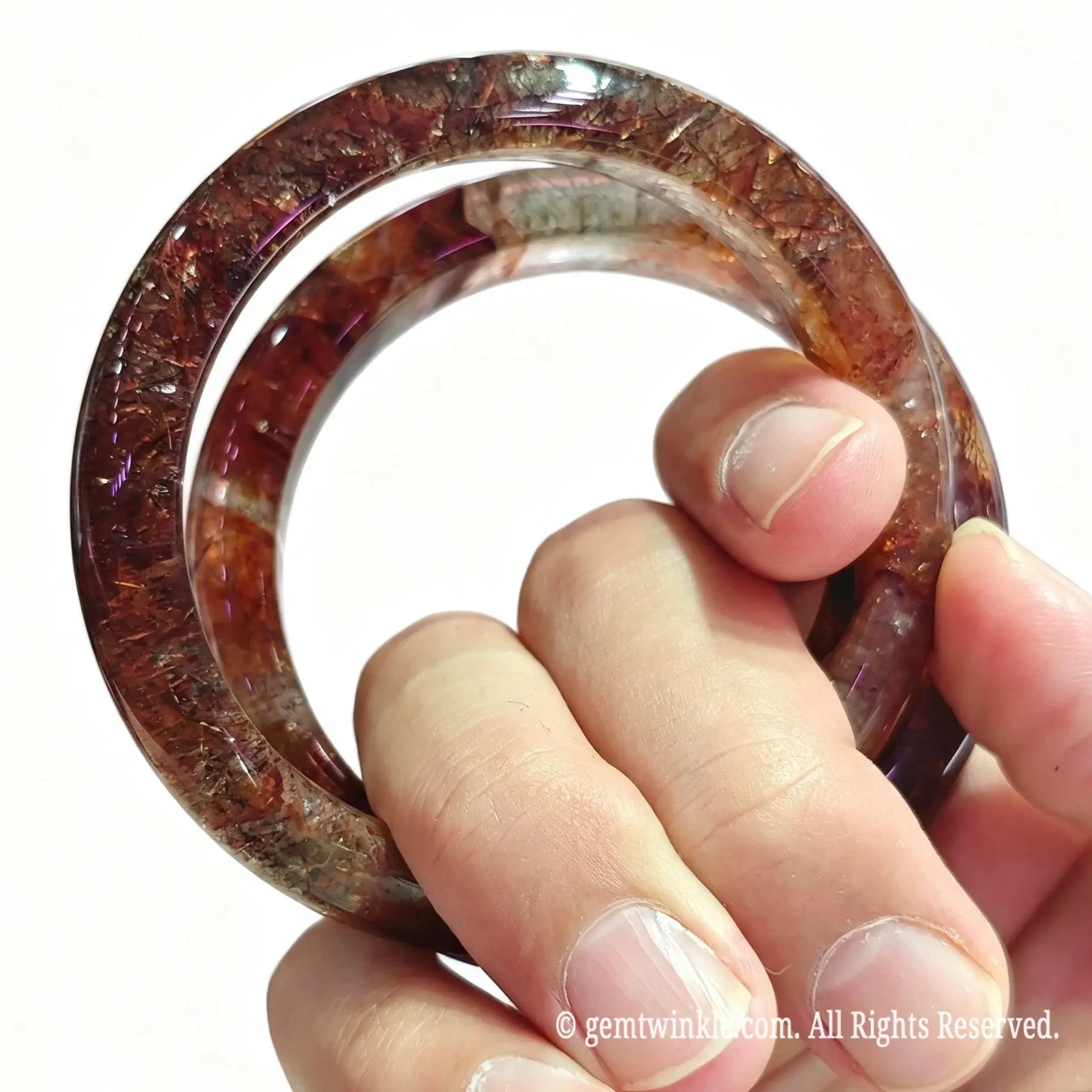 Angled hand view of solid super 7 quartz crystal bangles showcasing dark golden flash and smooth inner contour