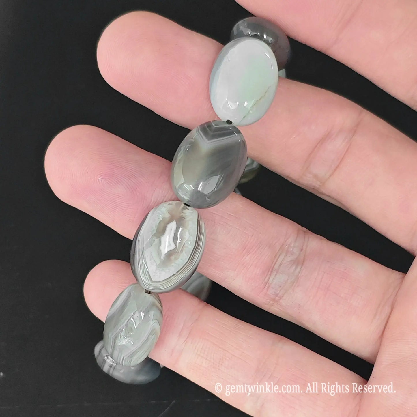 top view of natural swirl pattern grey agate oval bead bangle held in palm