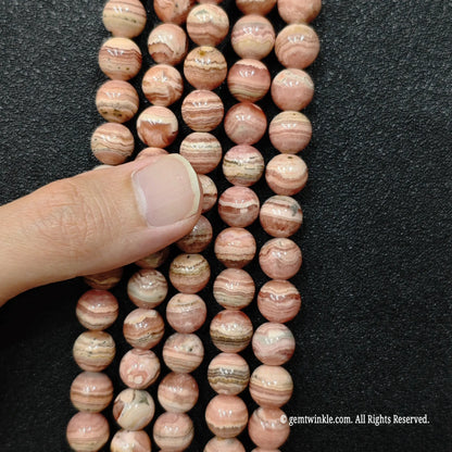 Large pink crystal beads in ten and twelve millimeter sizes held in hand to demonstrate scale and rich banding