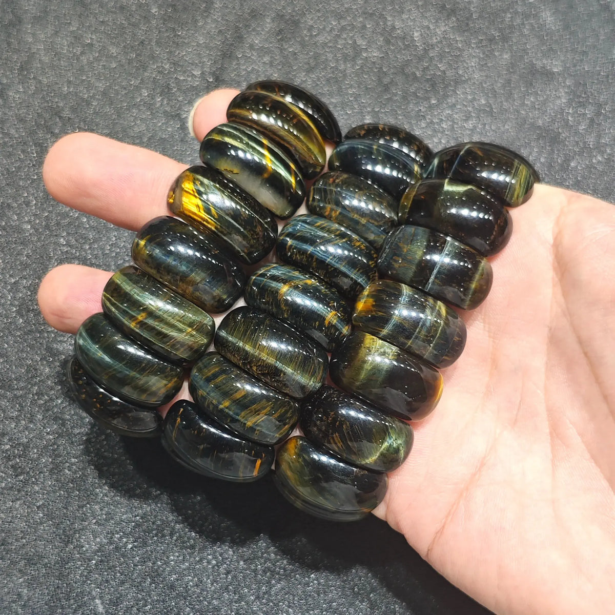 close up of three natural tiger eye barrel bead stretch bracelets stacked inside open palm showing smooth polished surfaces