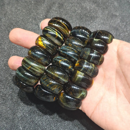close up of three natural tiger eye barrel bead stretch bracelets stacked inside open palm showing smooth polished surfaces