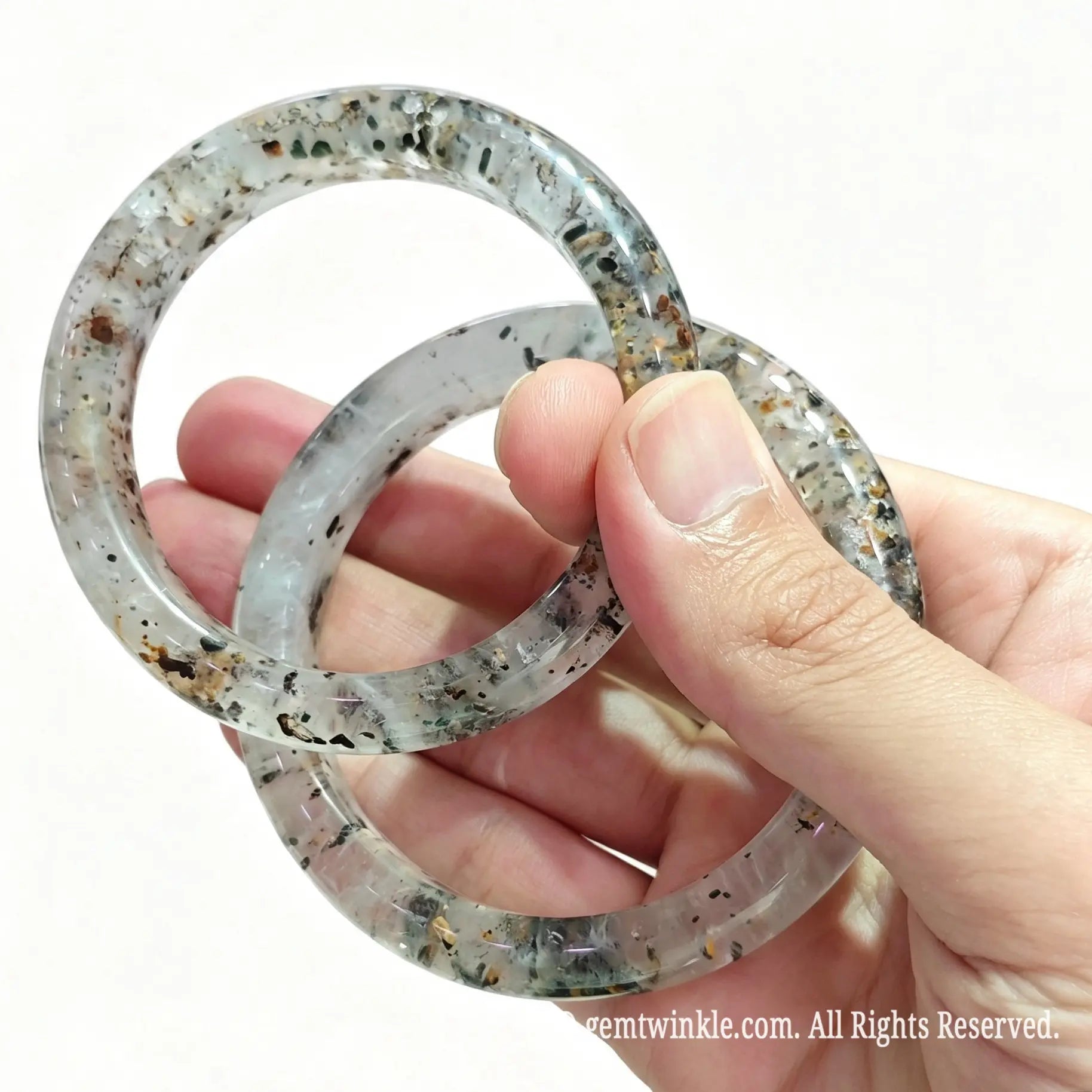Angled hand view of solid multi mineral quartz bangles showing bright glossy finish and dark tourmaline speckles