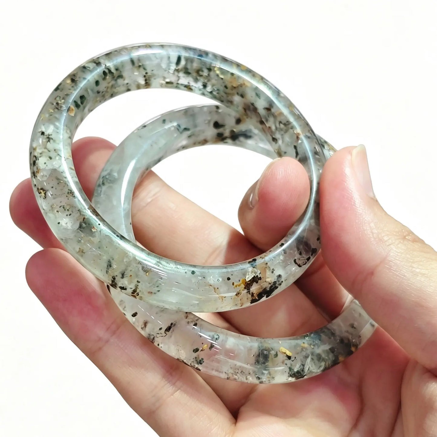Pair of smooth round three lives stone quartz bangles held in hand showing unique internal mineral inclusions