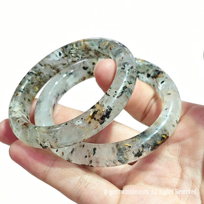 Stacked natural three lives stone quartz bangles resting on palm displaying clear crystal matrix and smooth inner ring