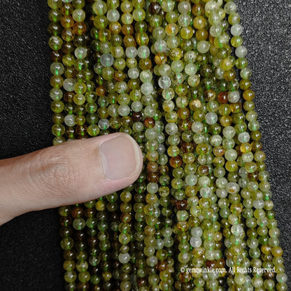 finger inspecting a bundle of delicate 3mm natural green garnet loose strands