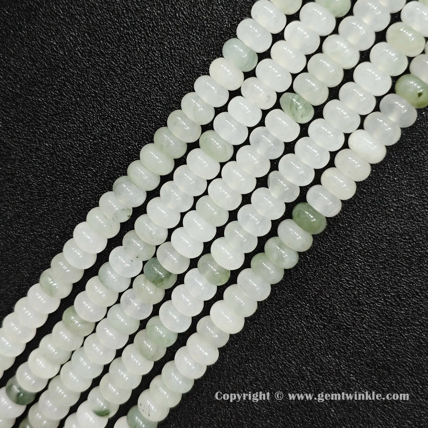 Angled view of natural tianshan jade smooth disc gemstone strands arranged parallel on dark background
