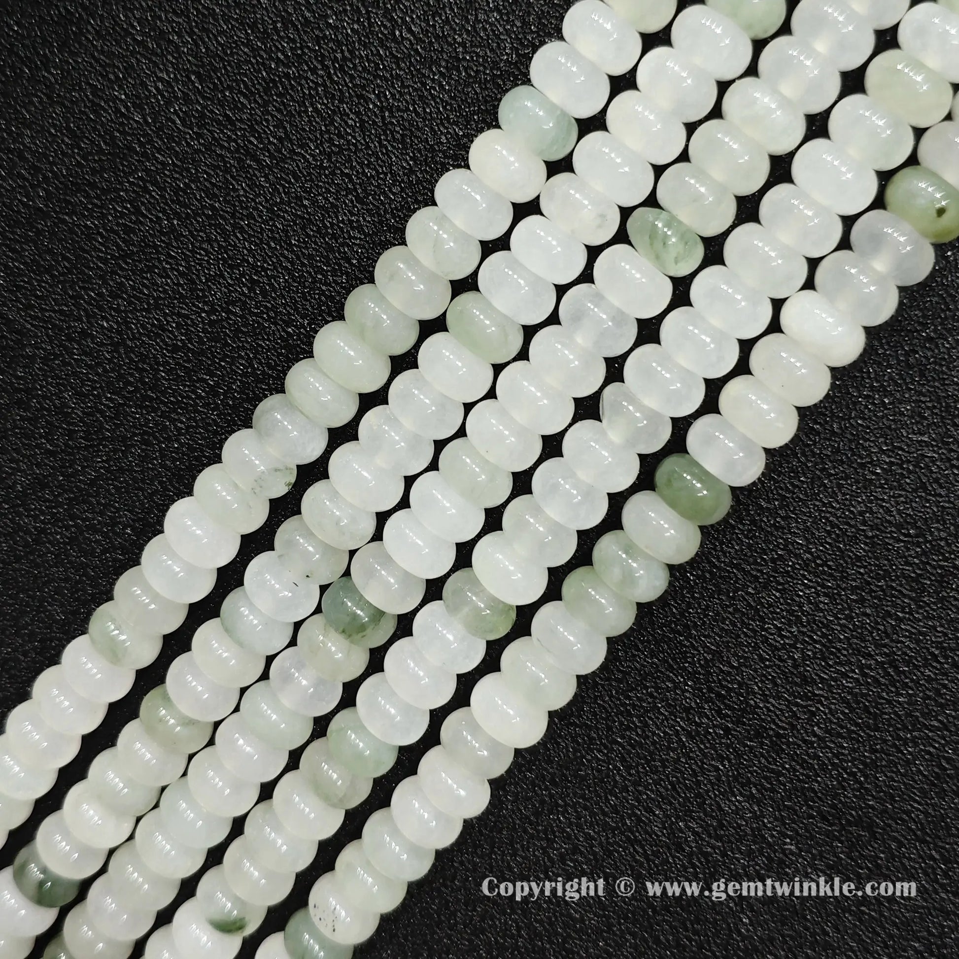 Angled view of natural tianshan jade smooth disc gemstone strands arranged parallel on dark background