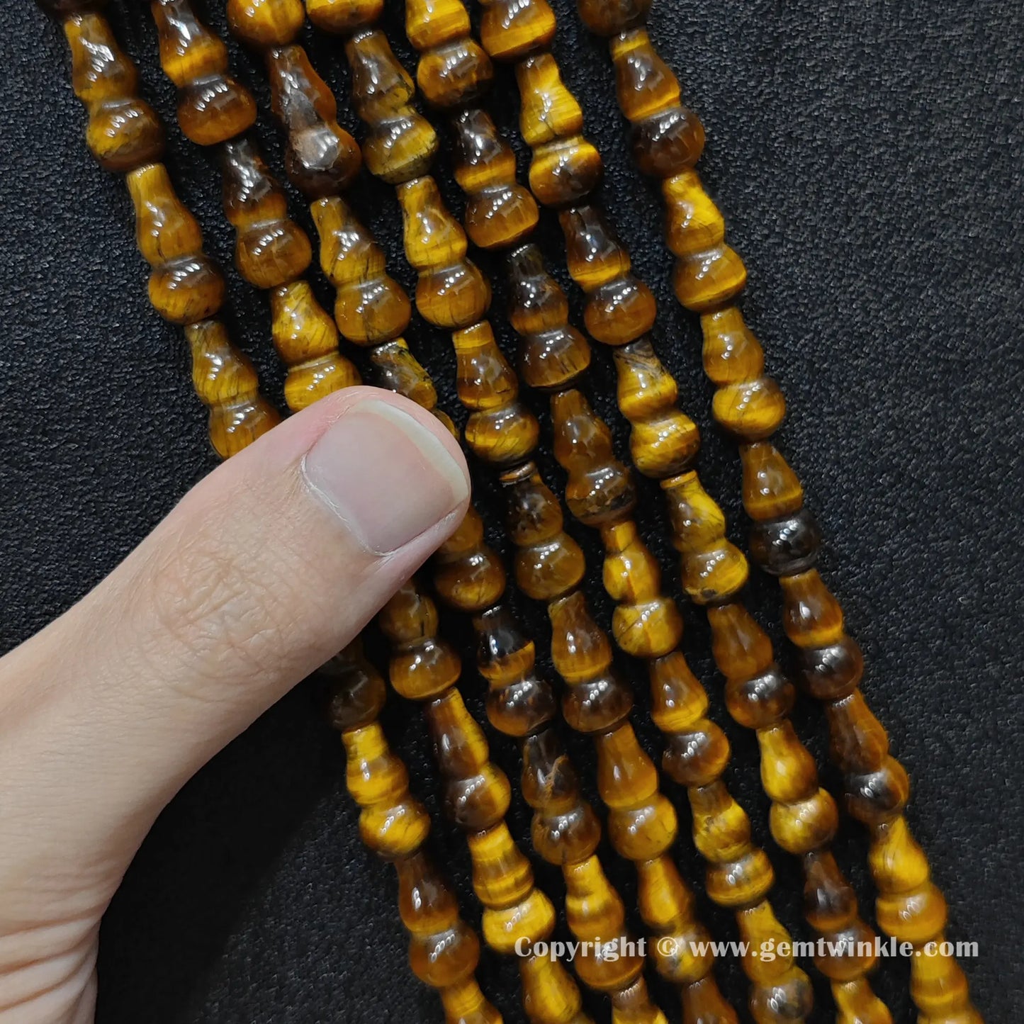 Close up view of natural yellow tiger eye calabash beads held on fingers for quality preview