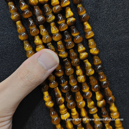 Close up view of natural yellow tiger eye calabash beads held on fingers for quality preview