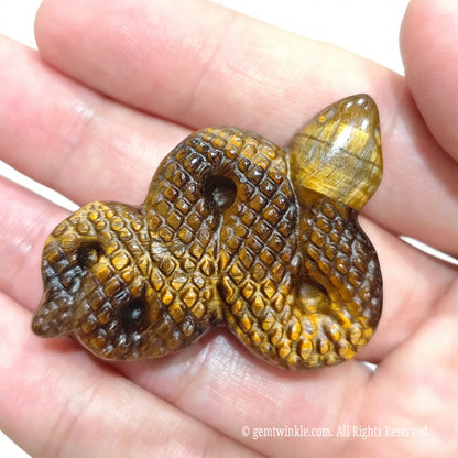 Side view of small tiger eye snake animal carving in hand displaying coiled body structure and polished surface