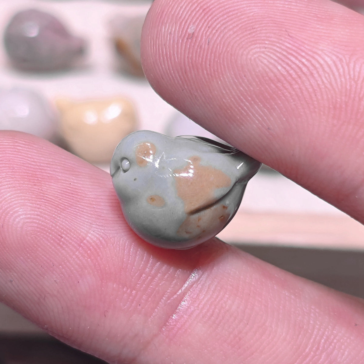 Front view of a tiny stone bird figurine with sweet expression resting between fingers