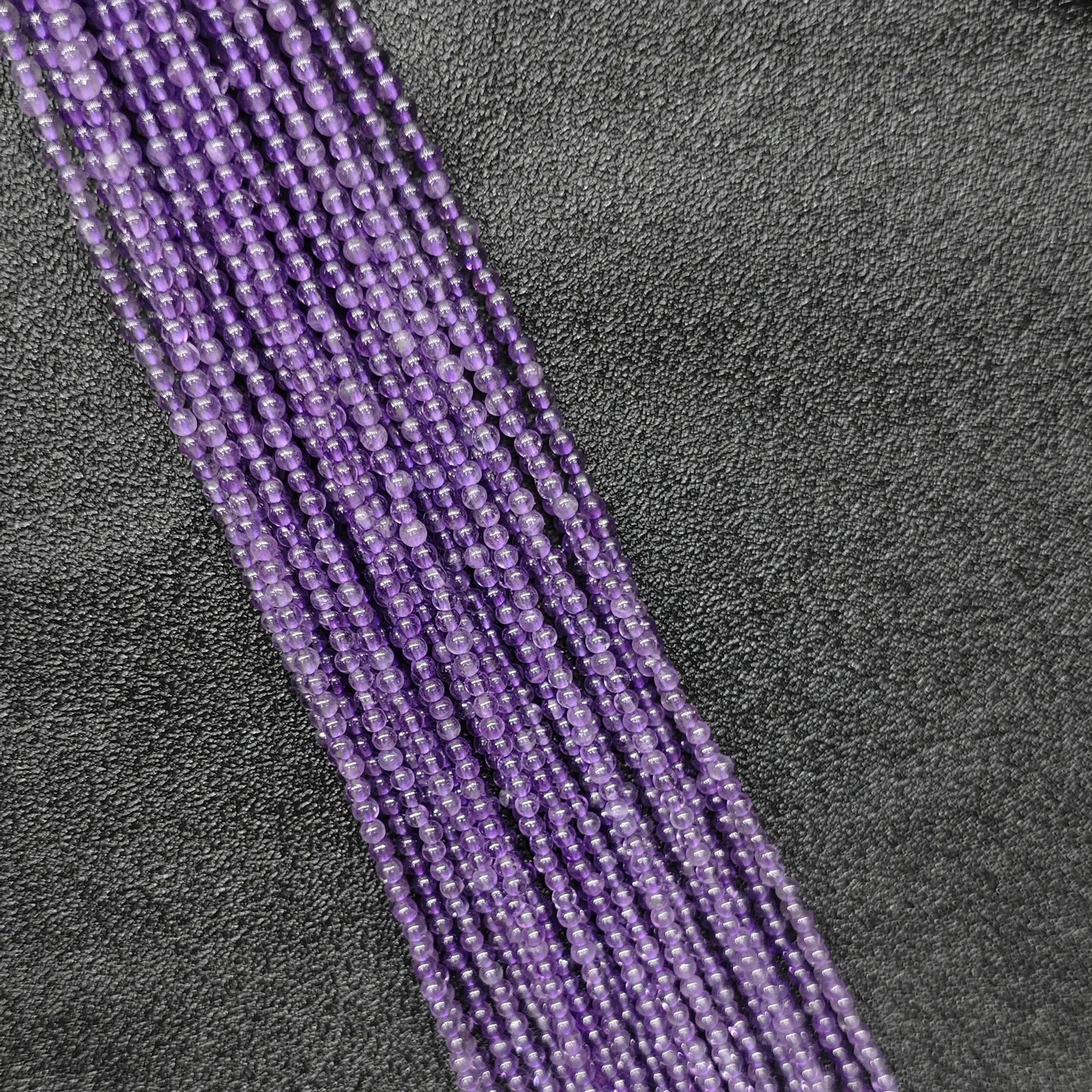 Macro closeup of tiny purple amethyst smooth round beads 2mm showing translucent violet quartz clarity