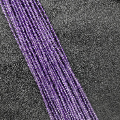 Macro closeup of tiny purple amethyst smooth round beads 2mm showing translucent violet quartz clarity