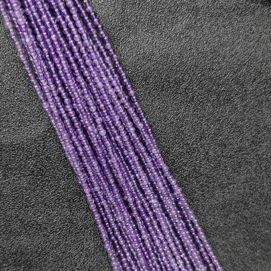 Macro closeup of tiny purple amethyst smooth round beads 2mm showing translucent violet quartz clarity