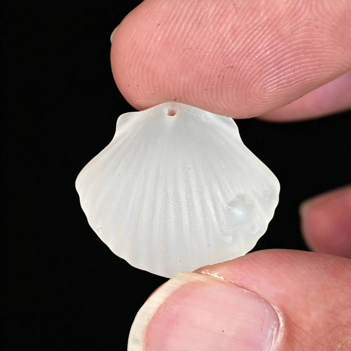 fingers holding frosted crystal shell pendant with drill hole