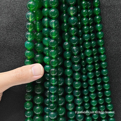 Multiple strands of green agate round beads held in hand for scale and size range verification