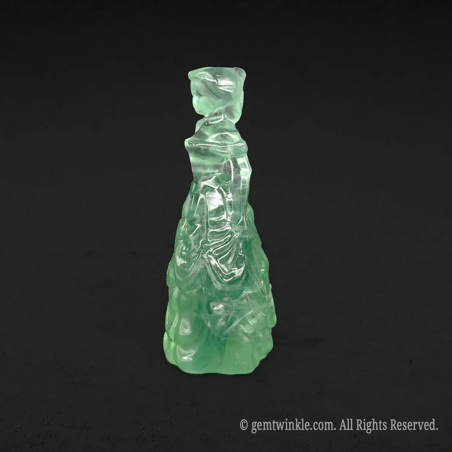 Side view of a translucent green fluorite queen figurine showing detailed dress ruffles and beautiful glass-like polish
