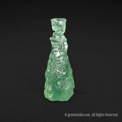 Side view of a translucent green fluorite queen figurine showing detailed dress ruffles and beautiful glass-like polish