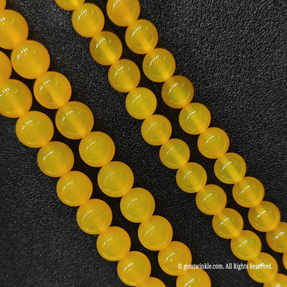 Diagonal view of translucent yellow chalcedony round beads showcasing rich uniform saturation and smooth cut
