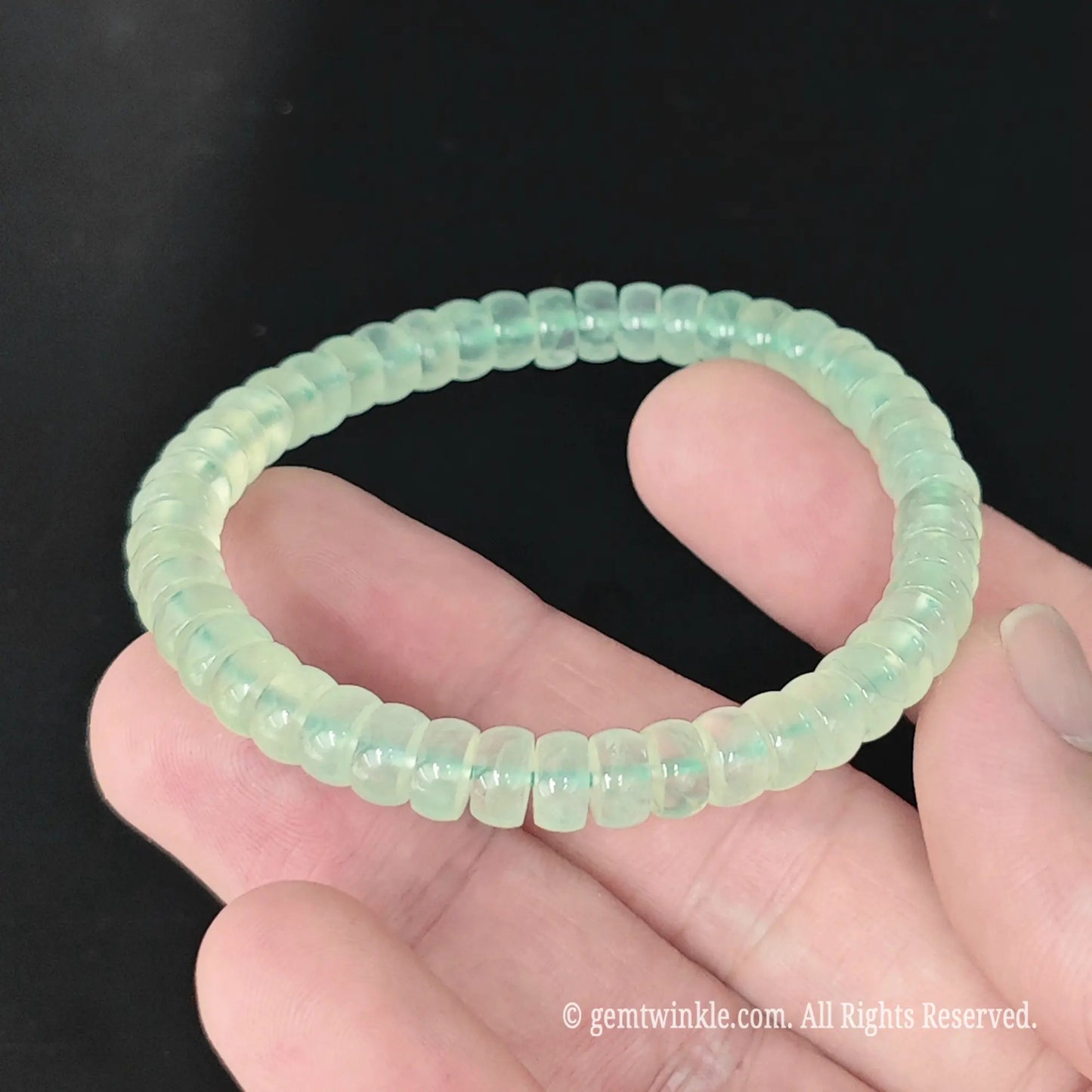 Translucent green prehnite disc bead stretch bracelet held in hand showing glossy wheel profile