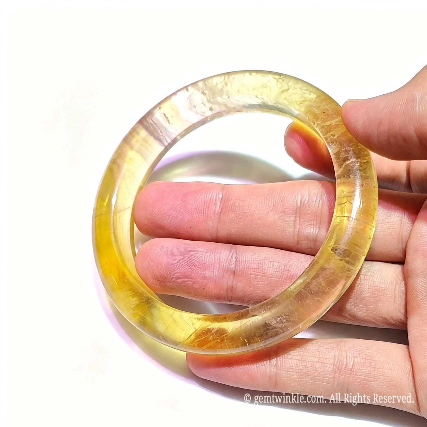 Translucent honey yellow fluorite bangle held up to light showing glowing crystal clarity and polished finish