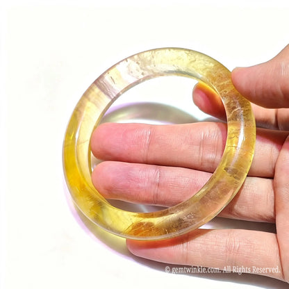 Translucent honey yellow fluorite bangle held up to light showing glowing crystal clarity and polished finish