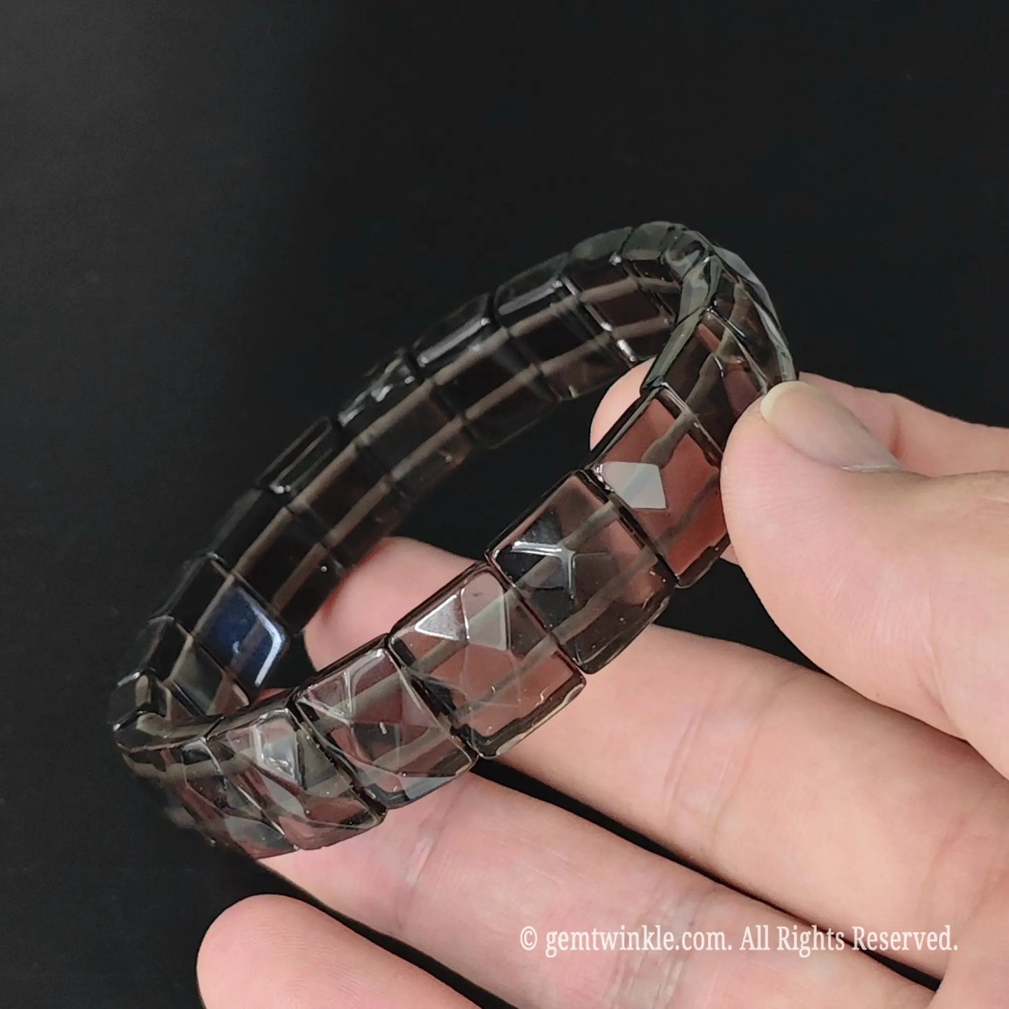 Overview of translucent obsidian geometric pyramid cut 11mm square bead bracelet resting on fingers