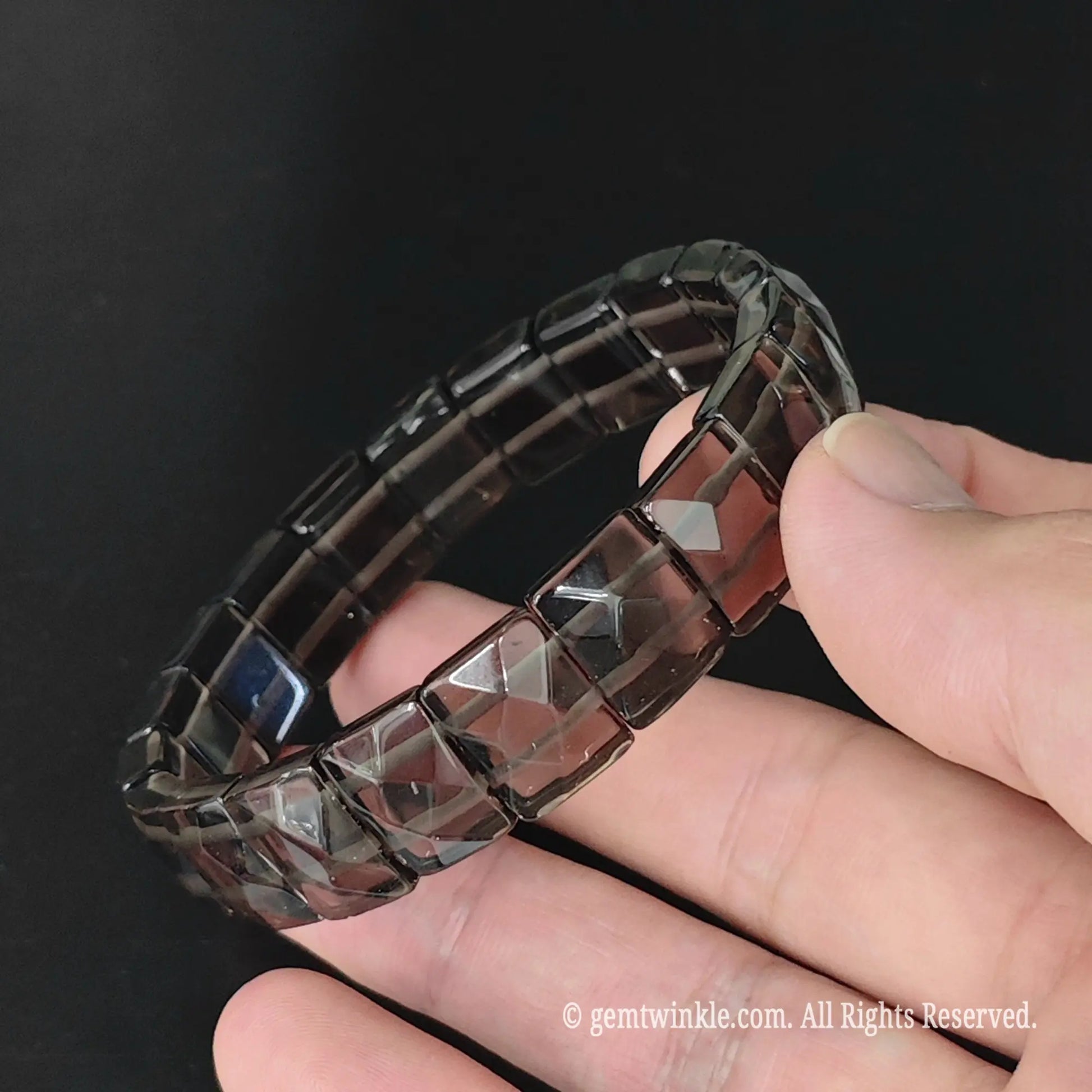 Overview of translucent obsidian geometric pyramid cut 11mm square bead bracelet resting on fingers