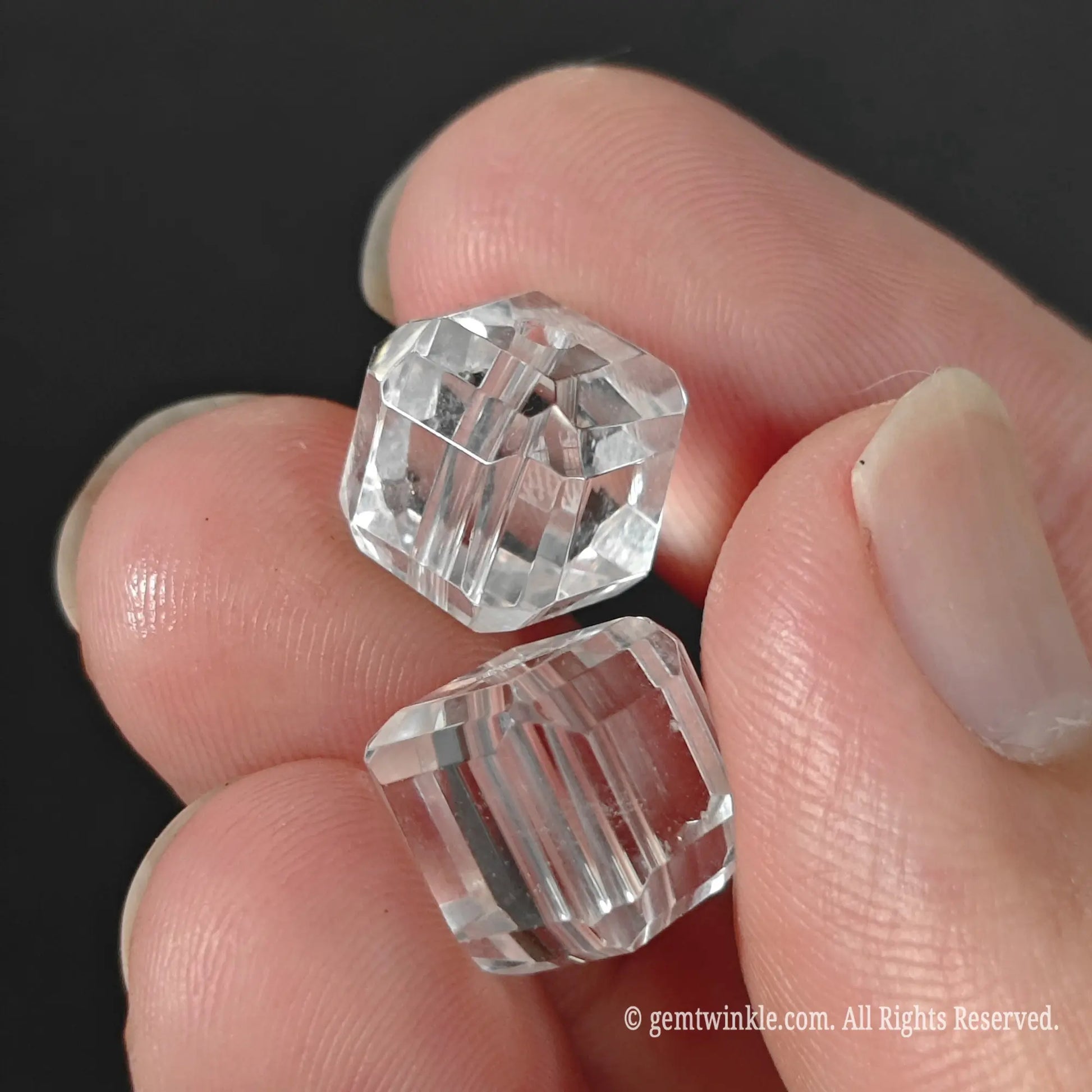 Transparent clear quartz cube gemstone beads pair held between fingers showcasing subtle natural veil lines