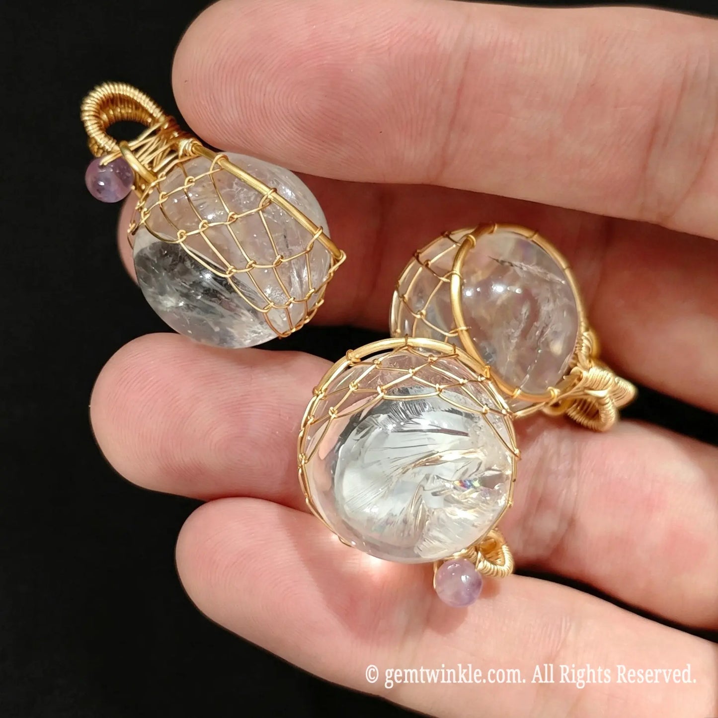Group view of 20mm clear quartz crystal ball pendants held in hand highlighting gold wire cage design for jewelry making