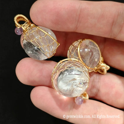 Group view of 20mm clear quartz crystal ball pendants held in hand highlighting gold wire cage design for jewelry making