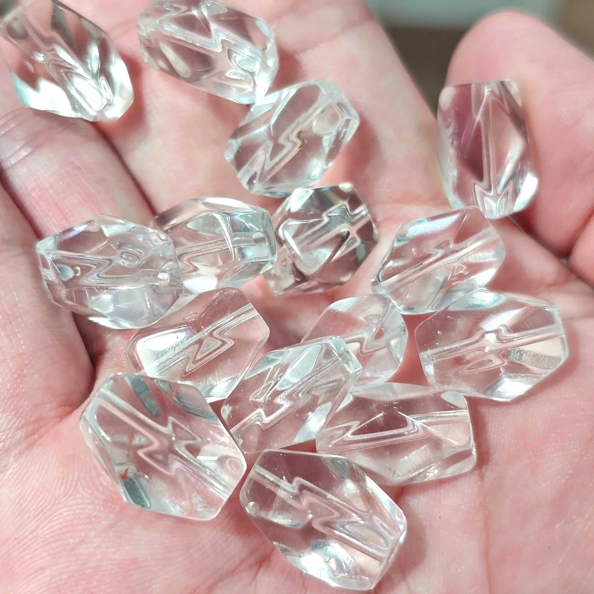 Hand holding multiple transparent quartz freeform beads highlighting drilled holes and internal natural veils