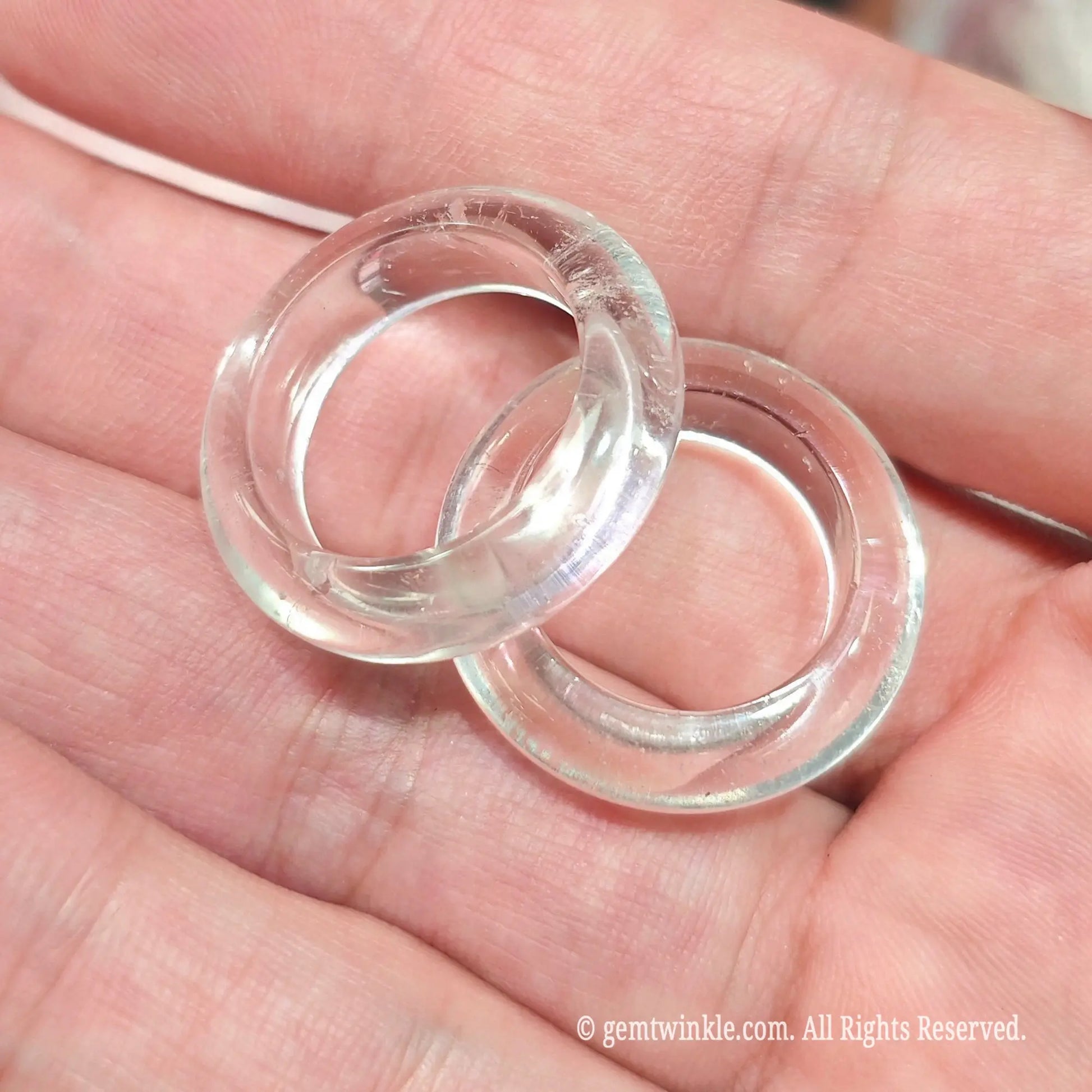Close up of transparent rock crystal gemstone band rings overlapping in hand highlighting clarity and smooth polish
