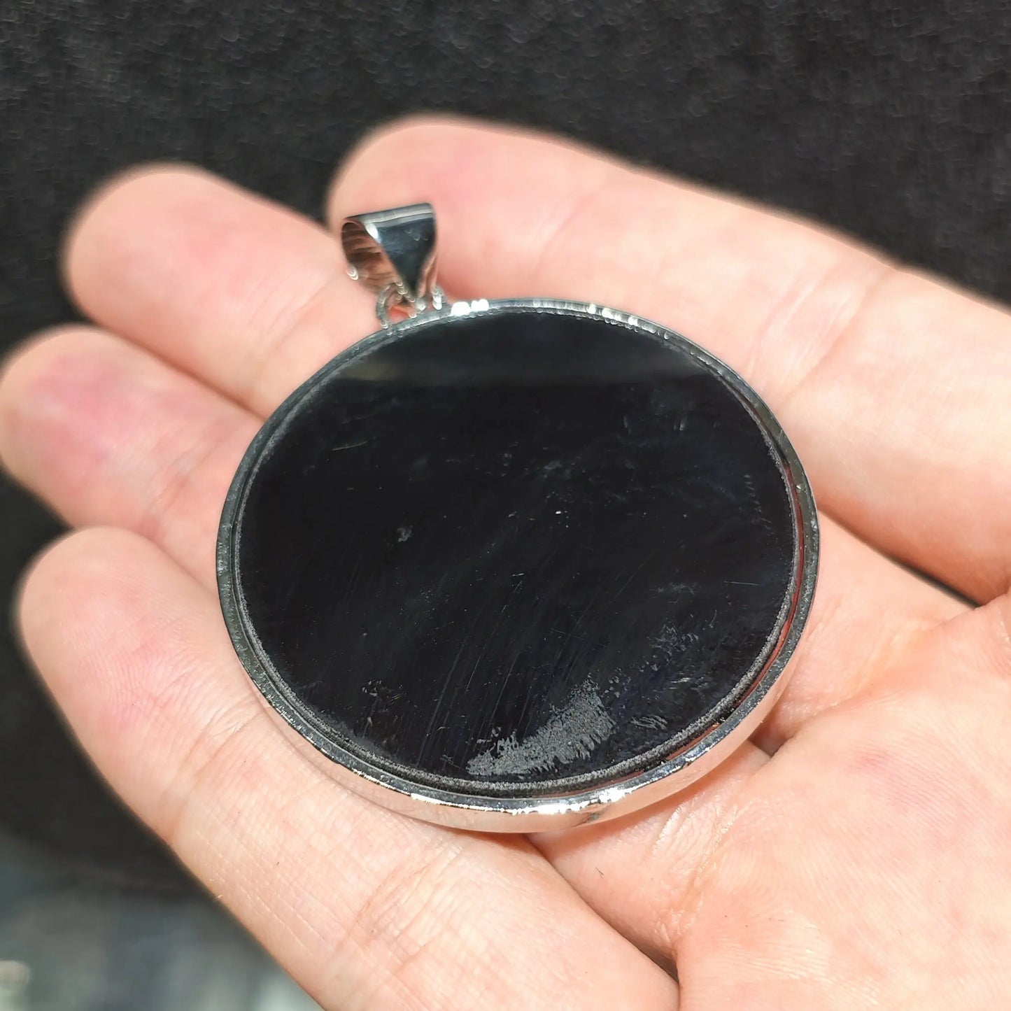 Back view display of large round Tree of Life abalone shell pendant showing smooth dark backing and silver tone bail loop