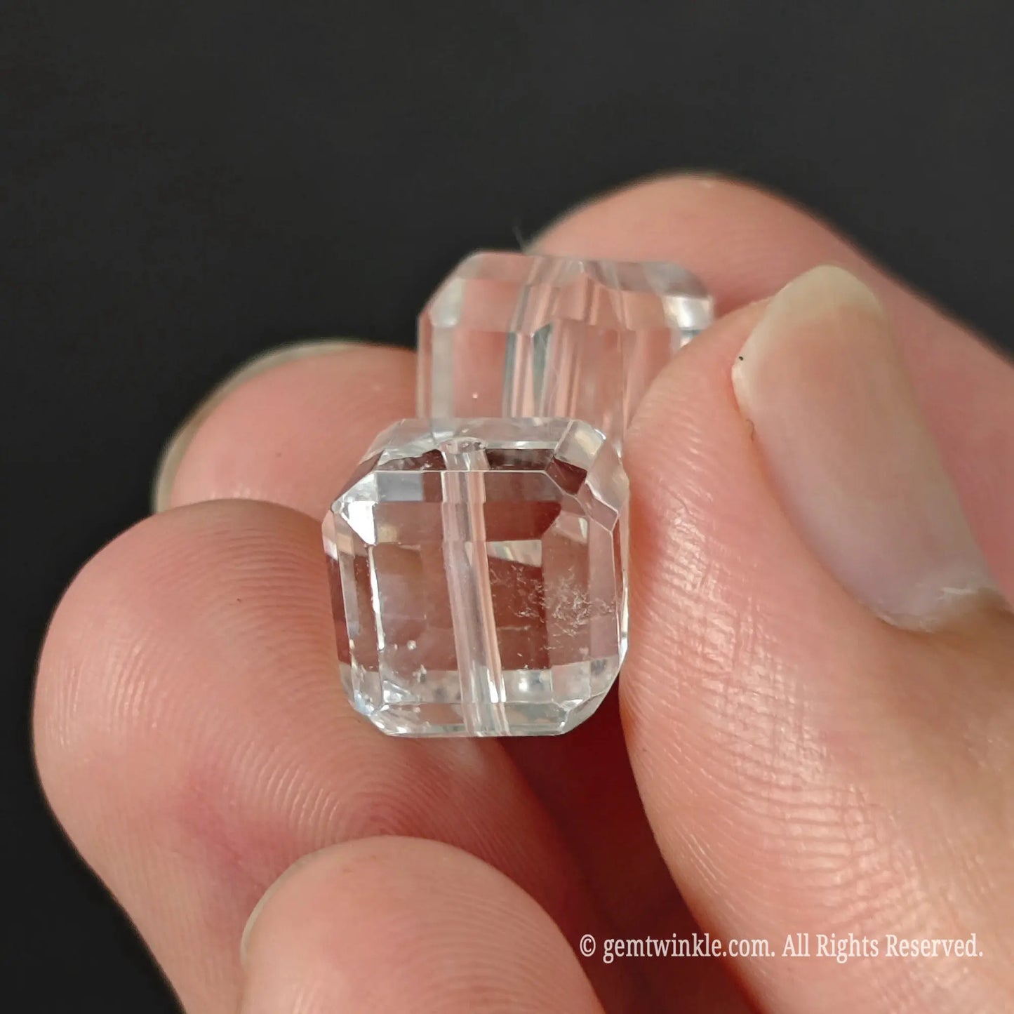 Two clear quartz faceted cube beads held in hand showing light refraction and clear crystal transparency