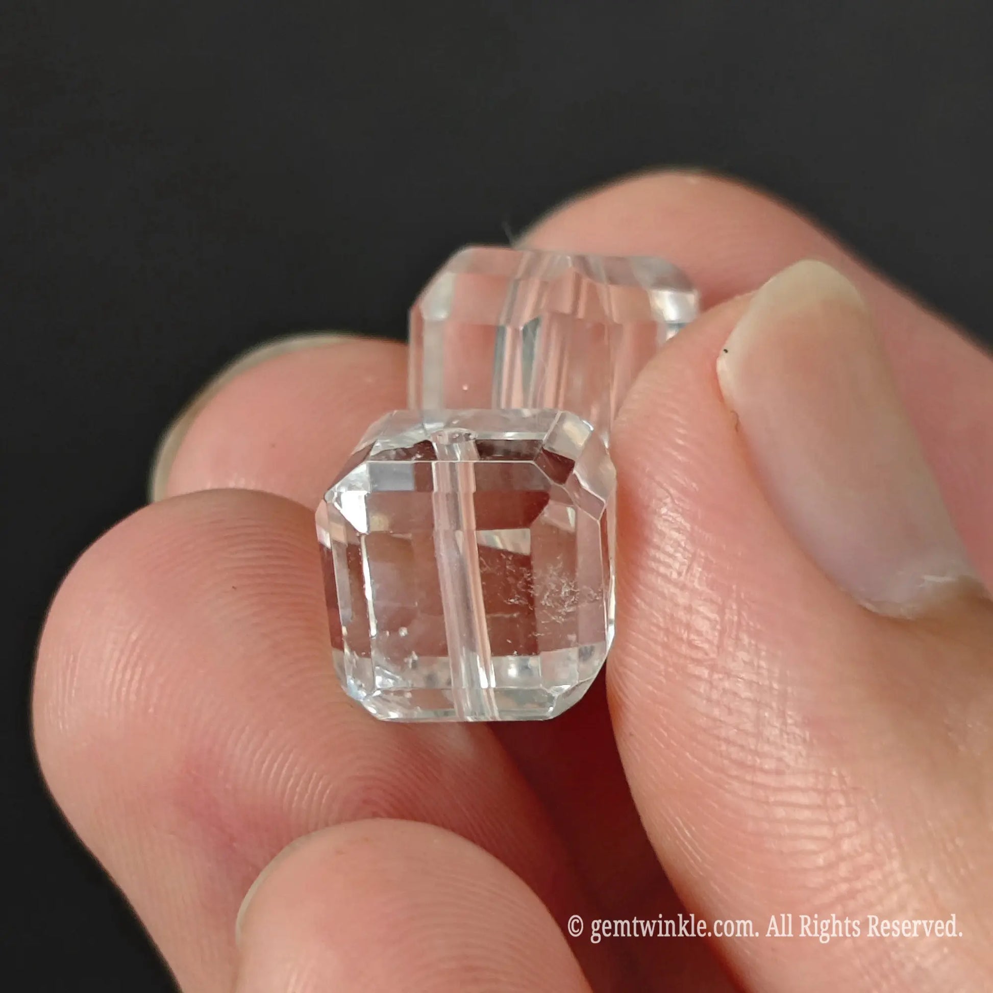 Two clear quartz faceted cube beads held in hand showing light refraction and clear crystal transparency