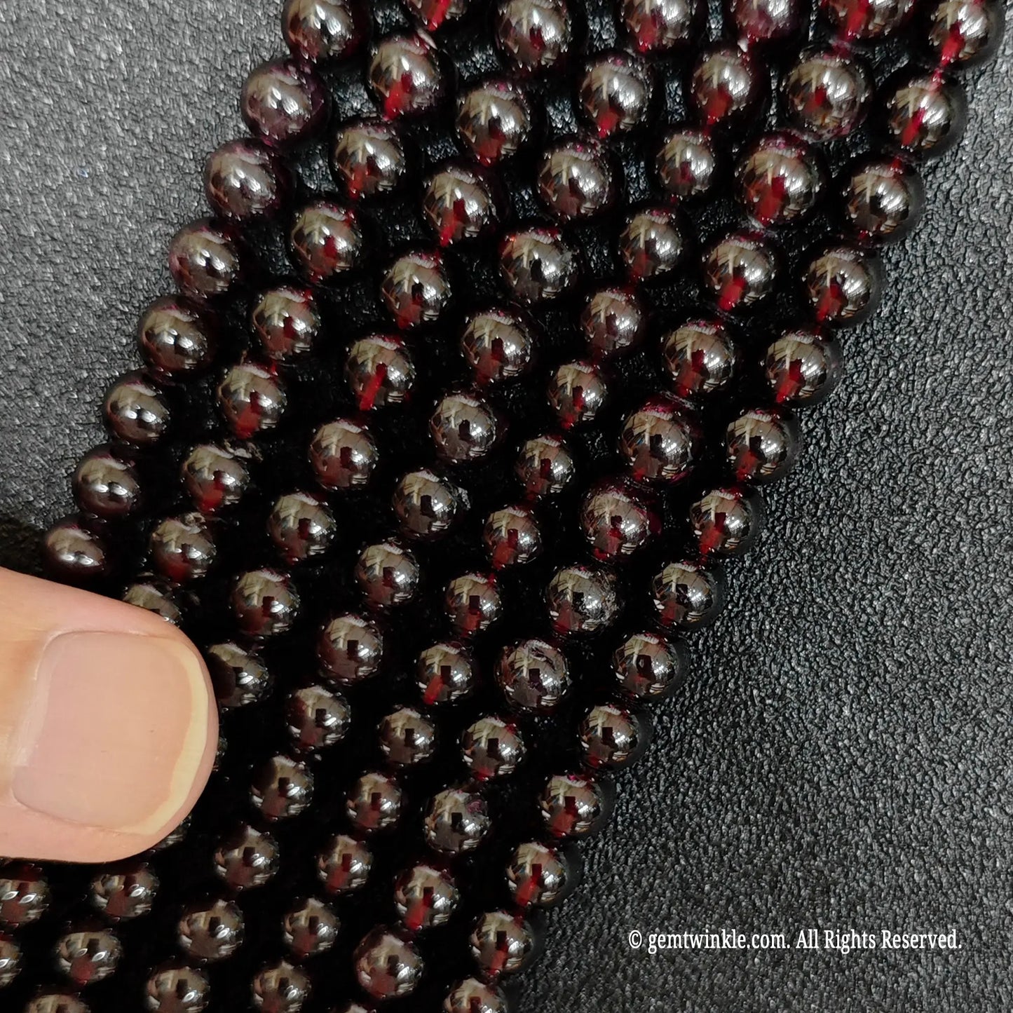finger pointing at thin vertical strands of small size garnet crystal beads