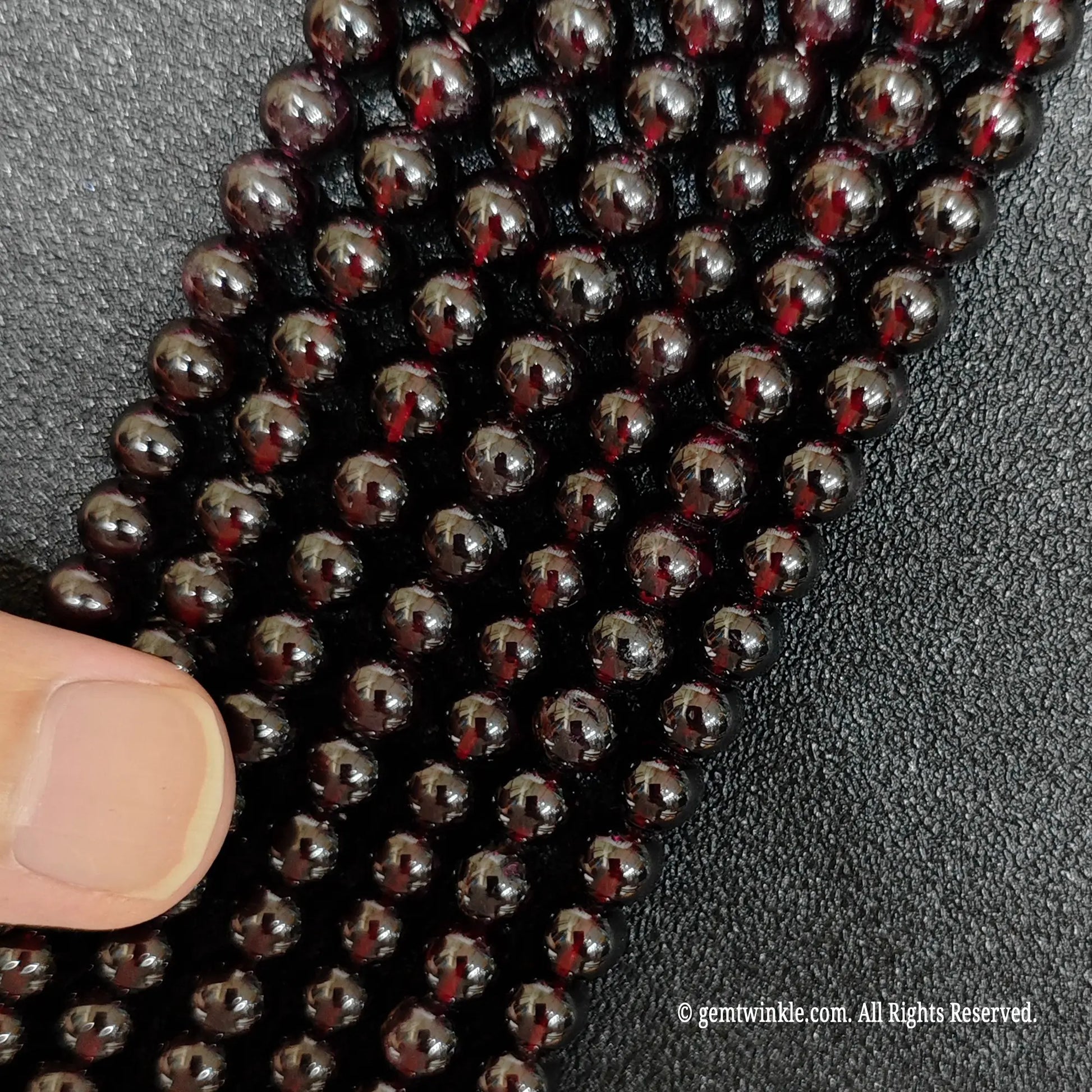 finger pointing at thin vertical strands of small size garnet crystal beads