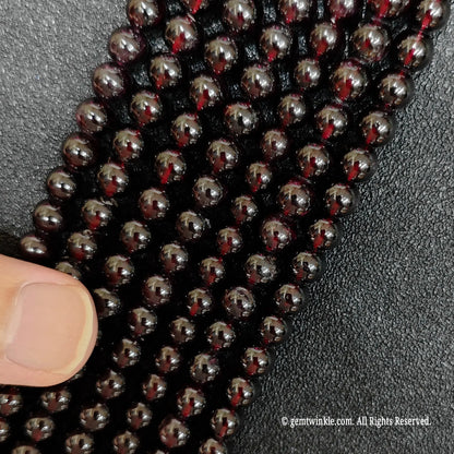 finger pointing at thin vertical strands of small size garnet crystal beads