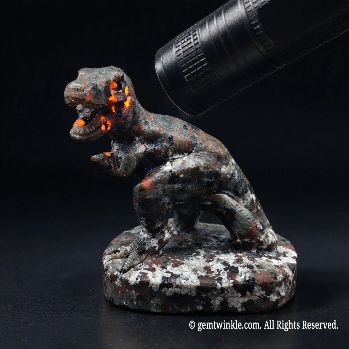 carved tyrannosaurus rex dinosaur statue showing fiery orange sodalite fluorescence under uv light torch