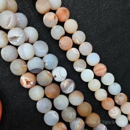 Four strands of natural un dyed matte agate geode beads showing organic earthy tones of grey ochre and cream colors on black background