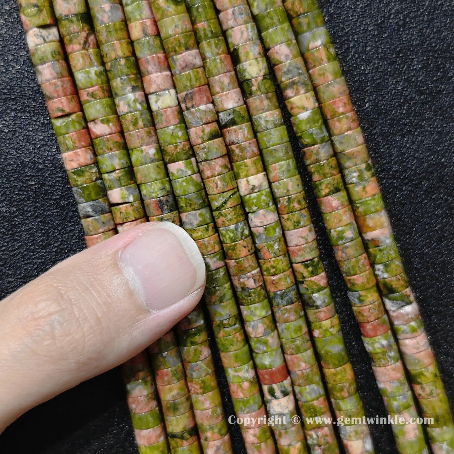 Close up view of 6x3mm unakite disc rondelle beads inspected on fingers for quality preview
