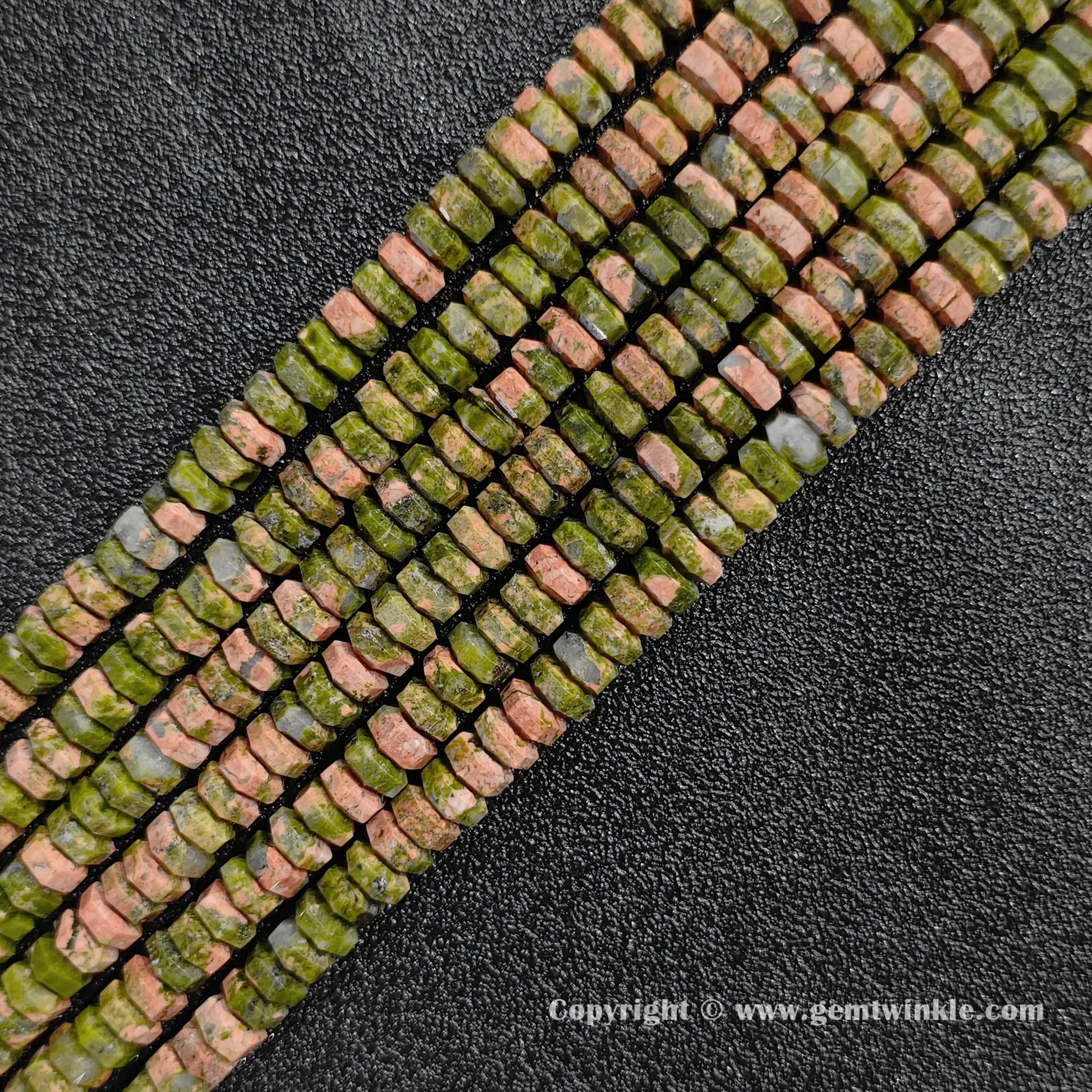 Angled view of natural unakite faceted disc gemstone strands arranged parallel on dark background