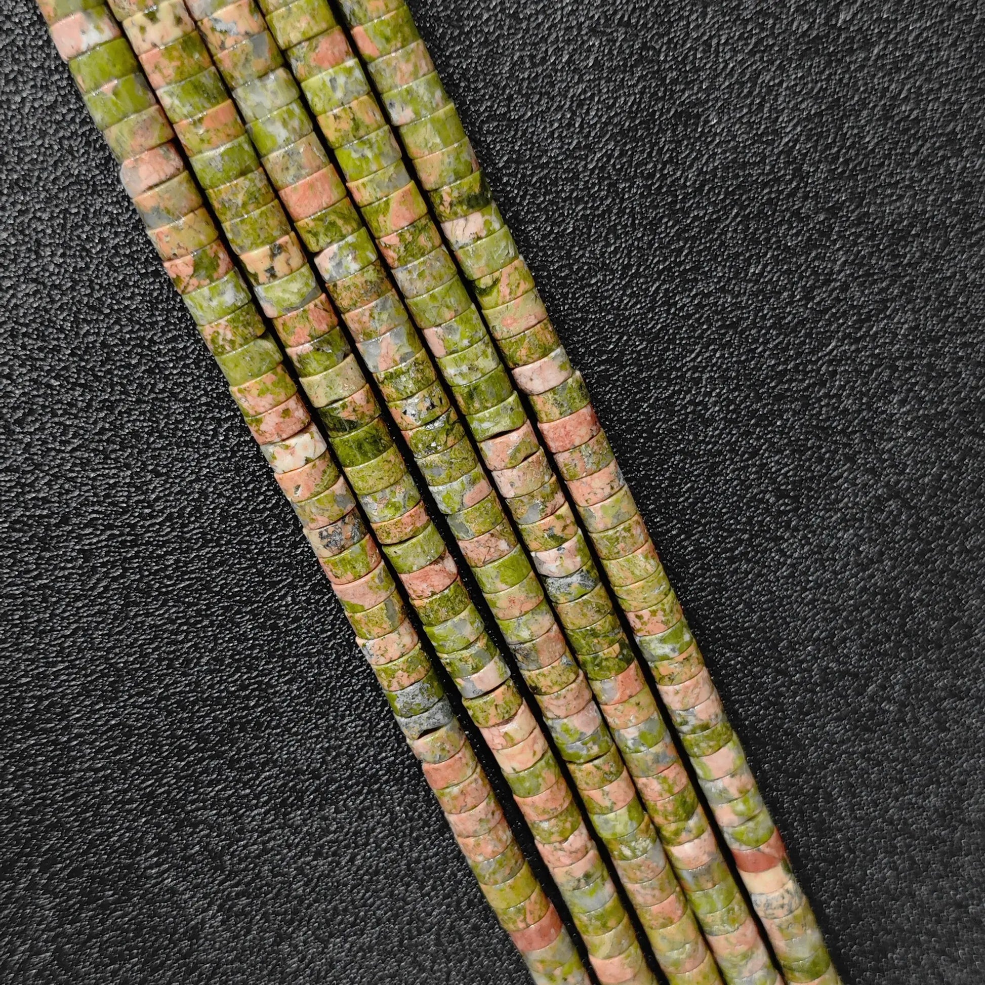 Macro closeup of natural unakite heishi rondelle beads 6x3mm showing green and pink mineral matrix