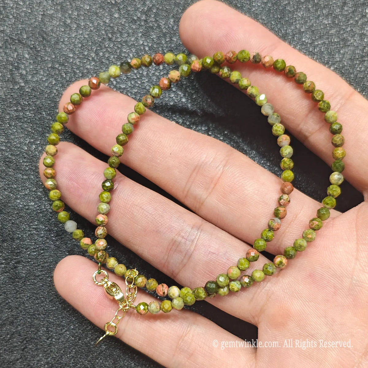 Hand holding 3mm faceted unakite necklace showing green epidote and pink feldspar matrix